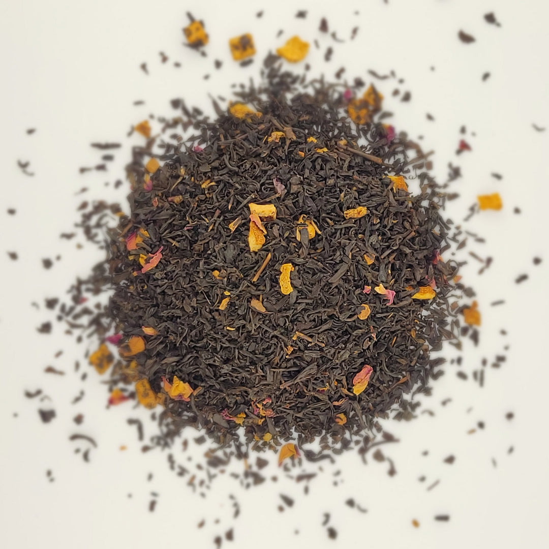 Dry black tea leaves with small orange and yellow pieces on a white background