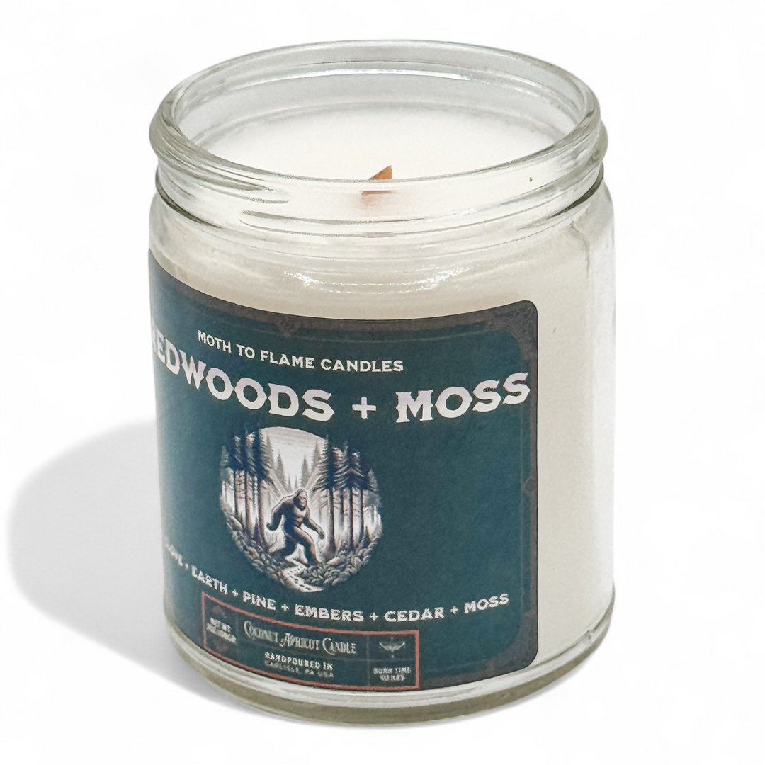 Candle in a glass jar with a label reading 'Woodlands + Moss' on a white background