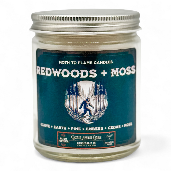 Candle jar labeled 'Redwoods + Moss' with a blue label and silver lid on a white background.